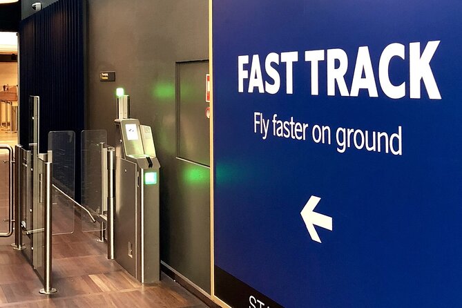 Fast Track Blue sign reading 'FAST TRACK' with 'Fly faster on ground' and a left arrow, beside security barriers in an airport area.
